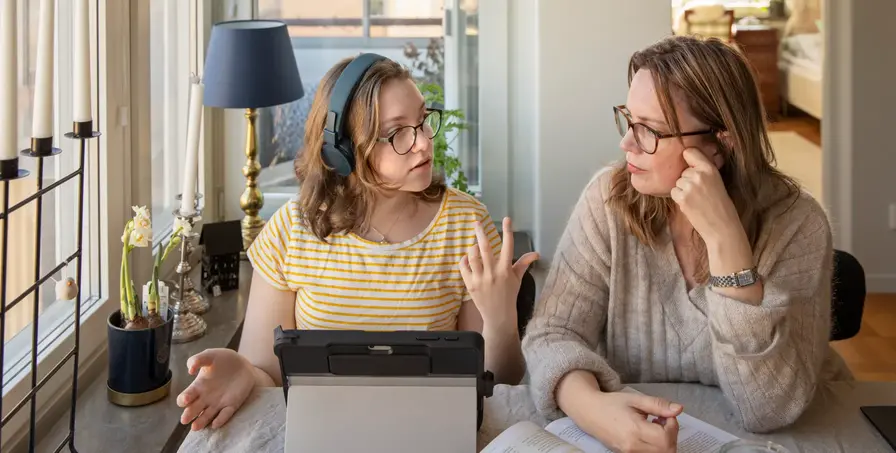 Tonåring och mamma sitter vid ett bord vid en dator och samtalar. 